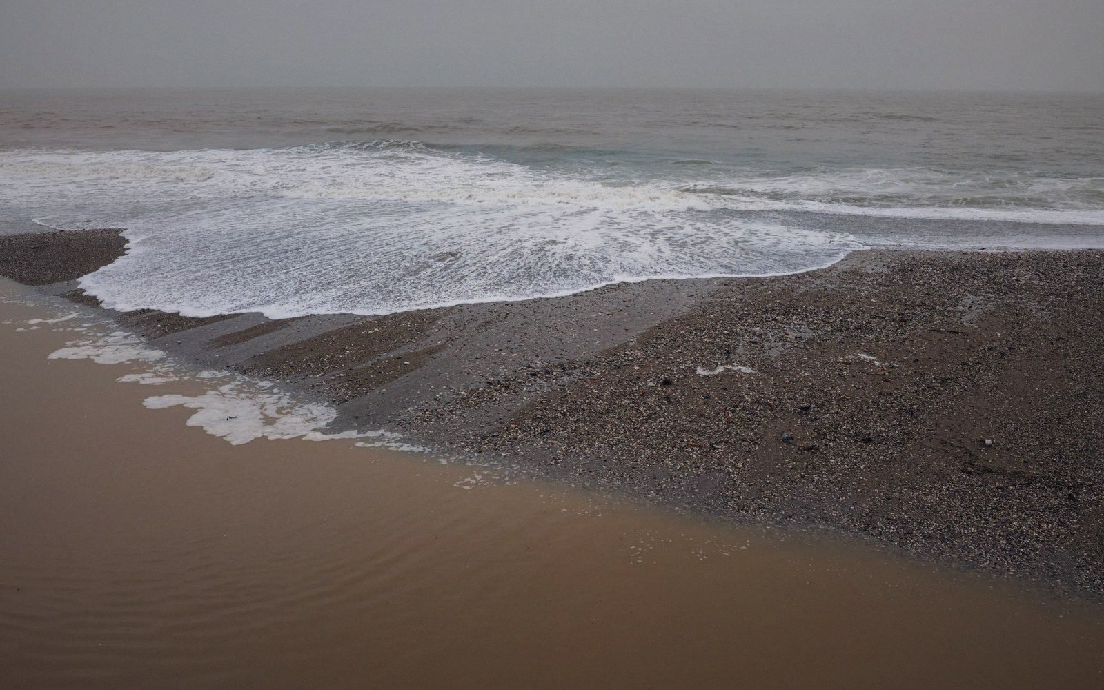 Waves wash onto a pebble and sand beach under overcast skies